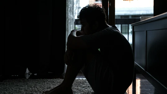 A depressed man sitting on the ground in the dark