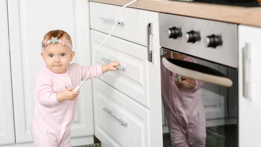 Little baby playing with electric plug in kitchen. Child in danger