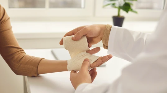 Doctor Bandaging Female Patient's Hand 