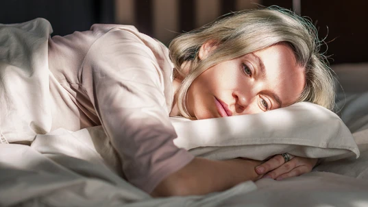 Woman lying awake on a bed, cuddling pillow, looking sad