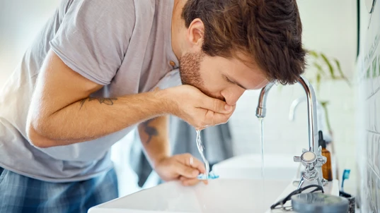 Man rinsing mouth while brushing teeth at bathroom sink