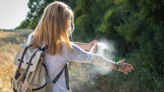 Woman spraying insect repellent on arm